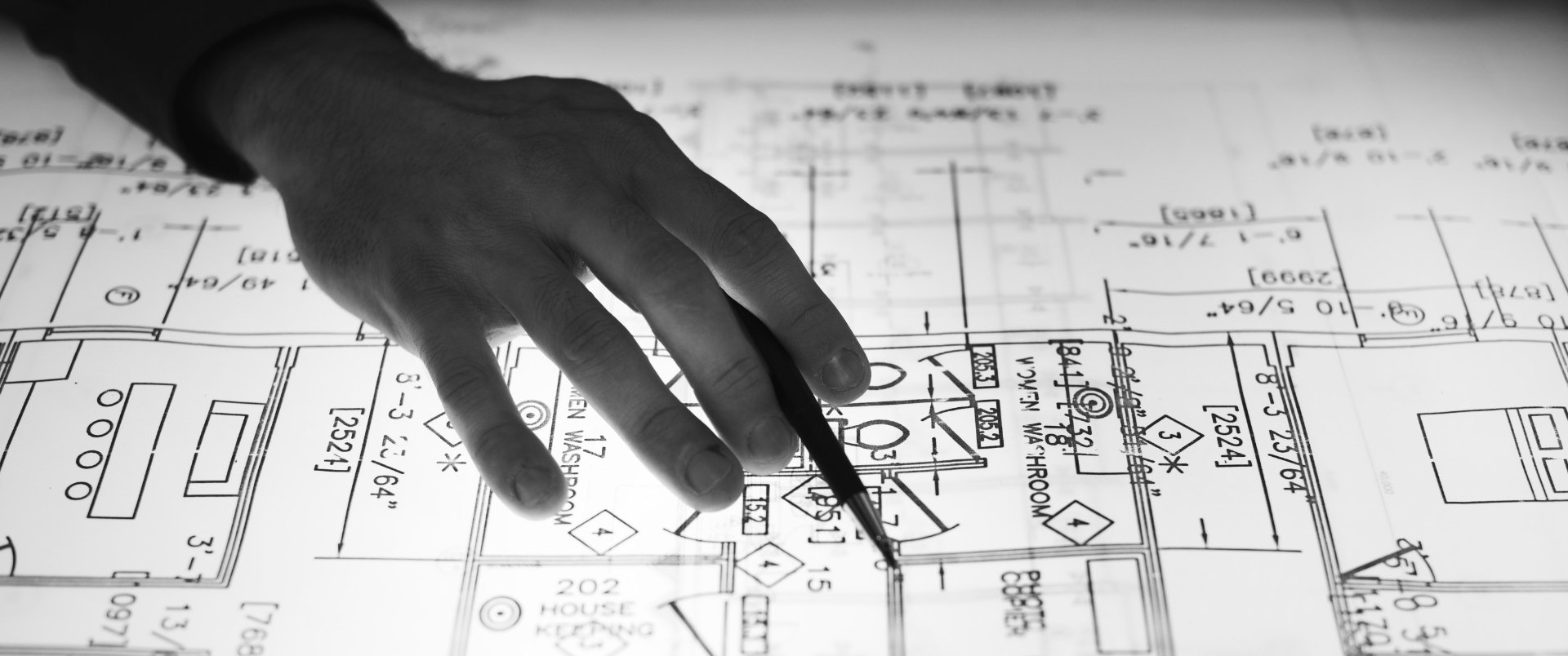 Hand with pencil hovering over blueprints — Real Estate Services